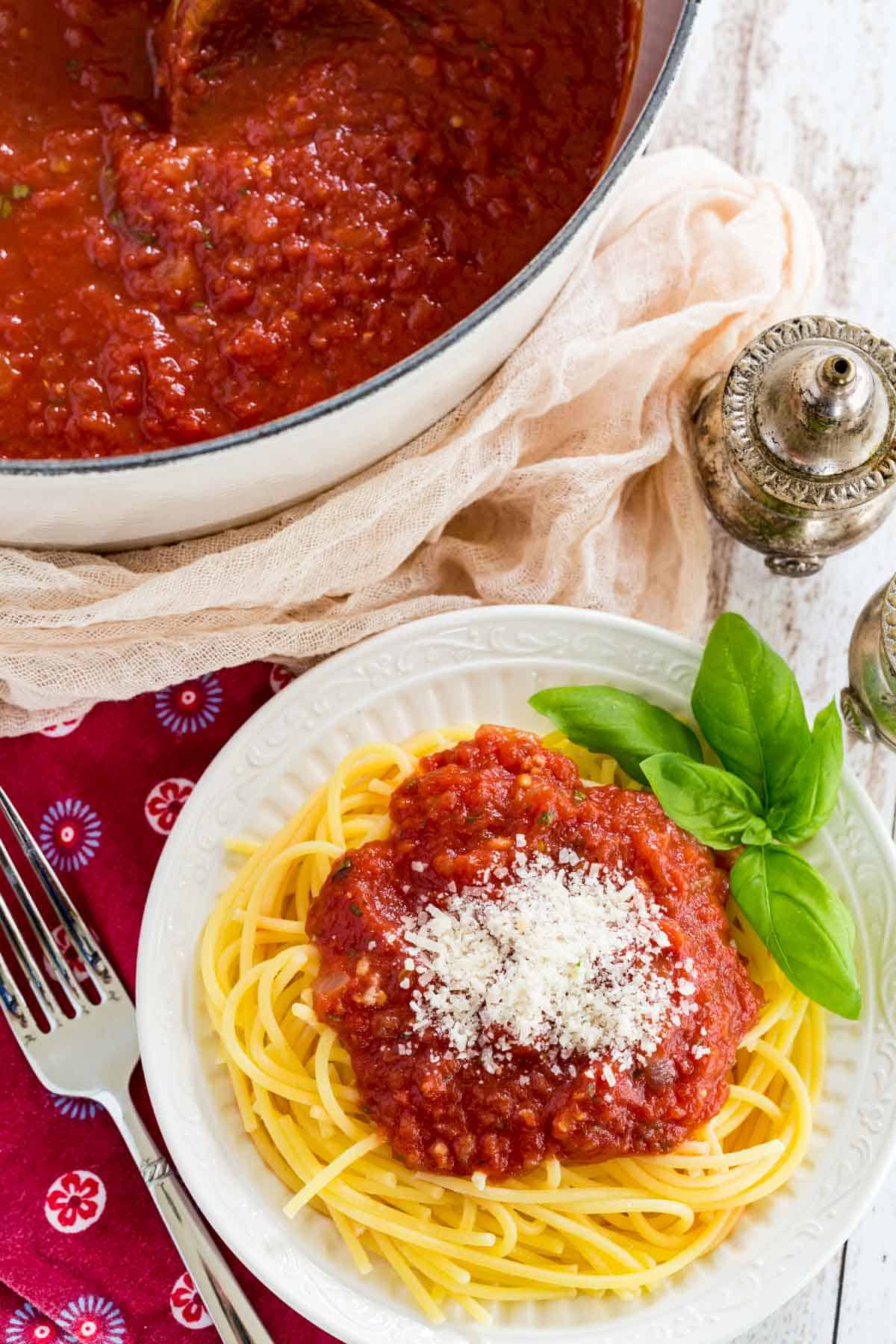 Spaghetti with homemade marinara sauce on a plate, next to a pot of sauce.