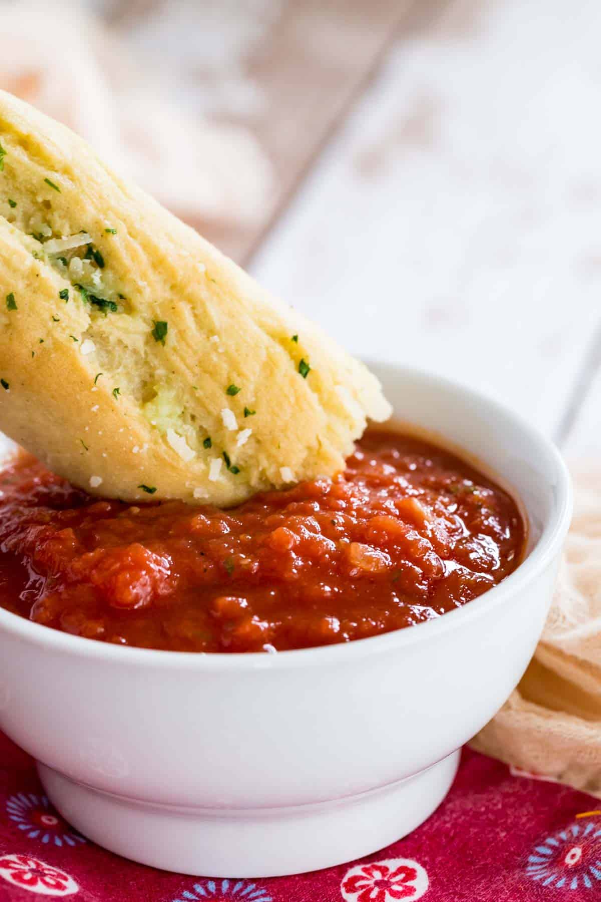A breadstick is dipped into a bowl of homemade marinara sauce.