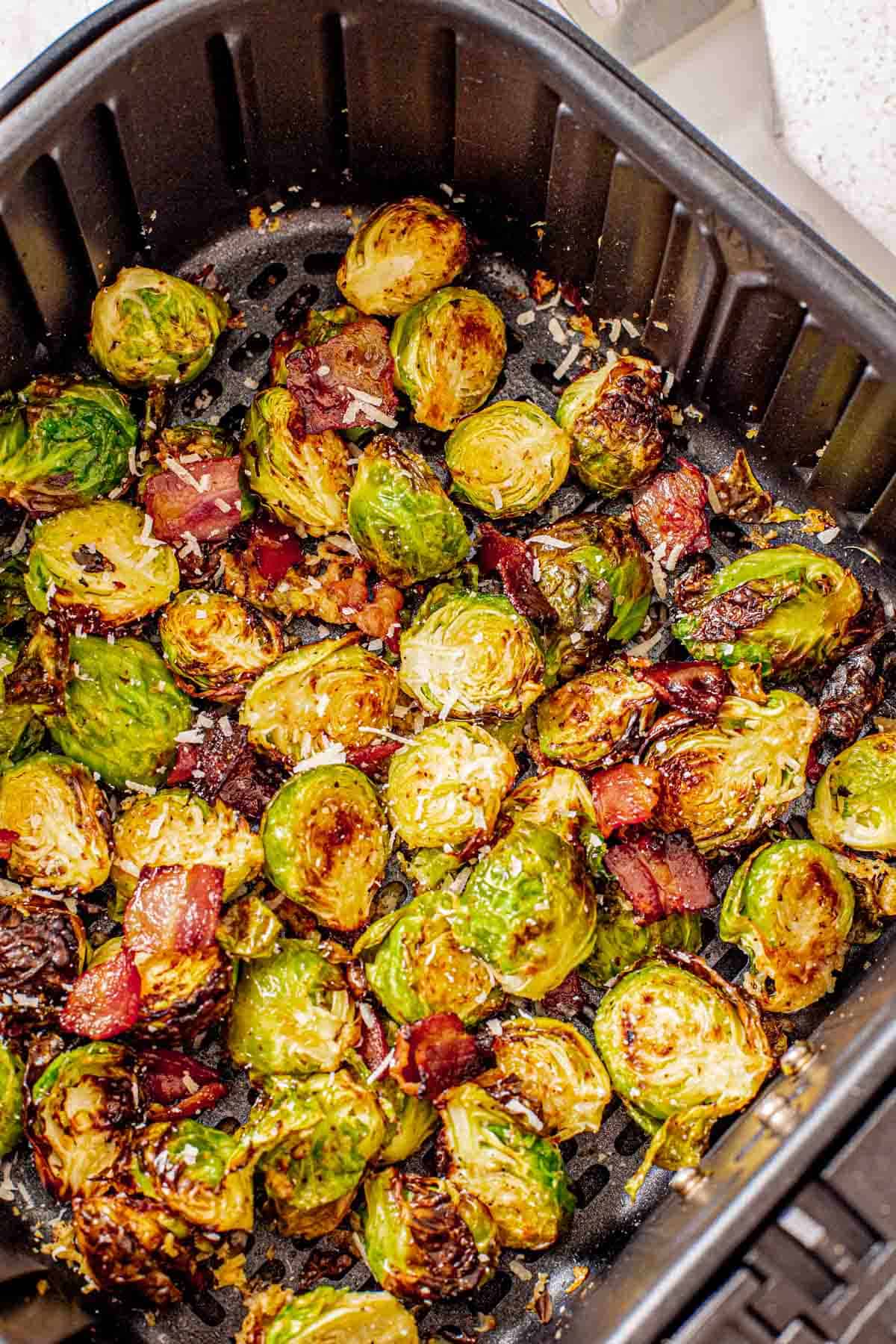 an air fryer basket with Brussels sprouts sprinkled with bacon and parmesan cheese