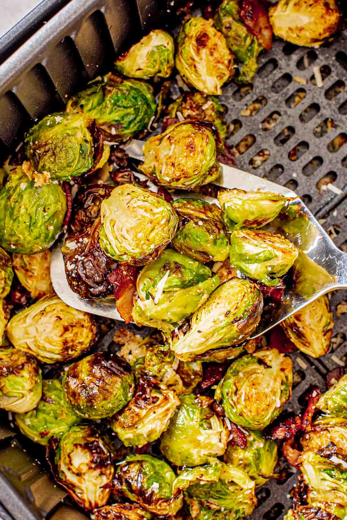 scooping Brussels sprouts out of the air fryer basket with a spatula