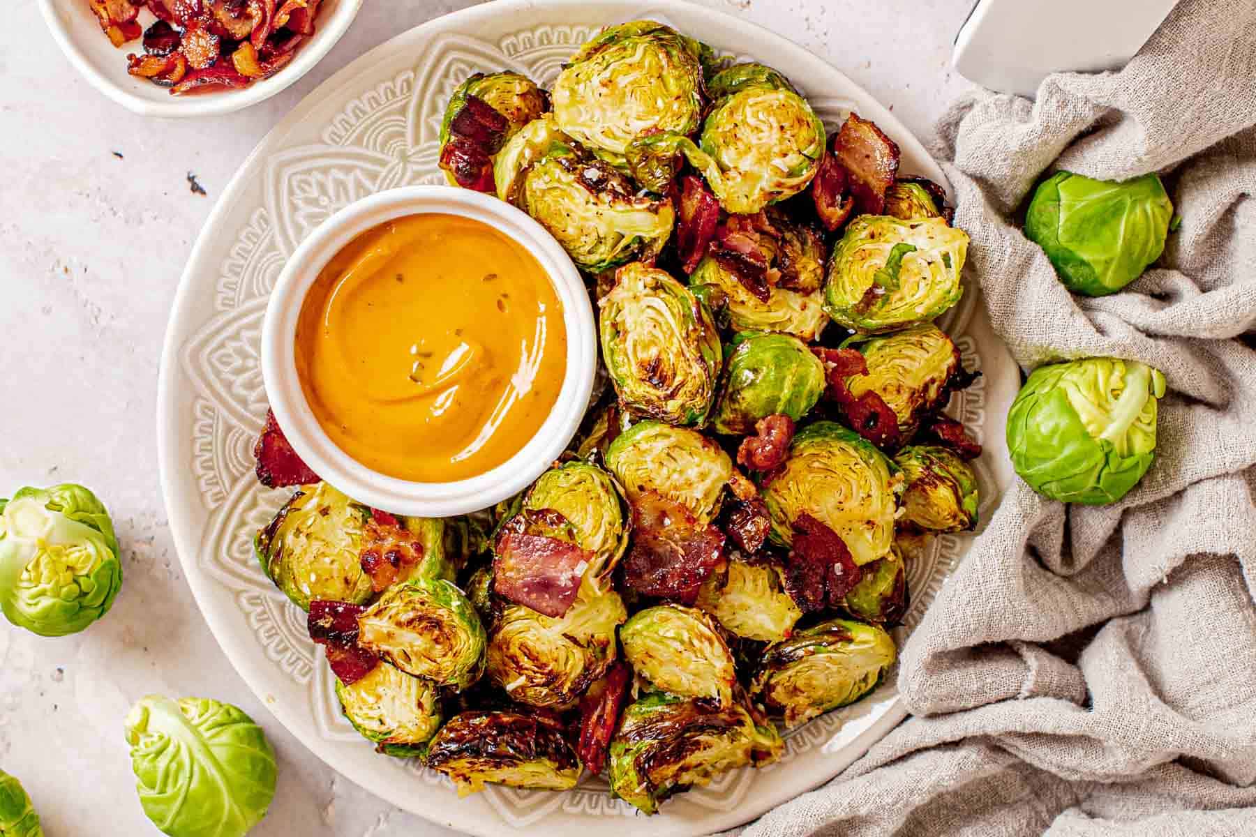 air fried Brussels sprouts with bacon on a plate with a bowl of dipping sauce
