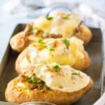 A serving tray holding three beef stuffed baked potatoes topped with cheese.