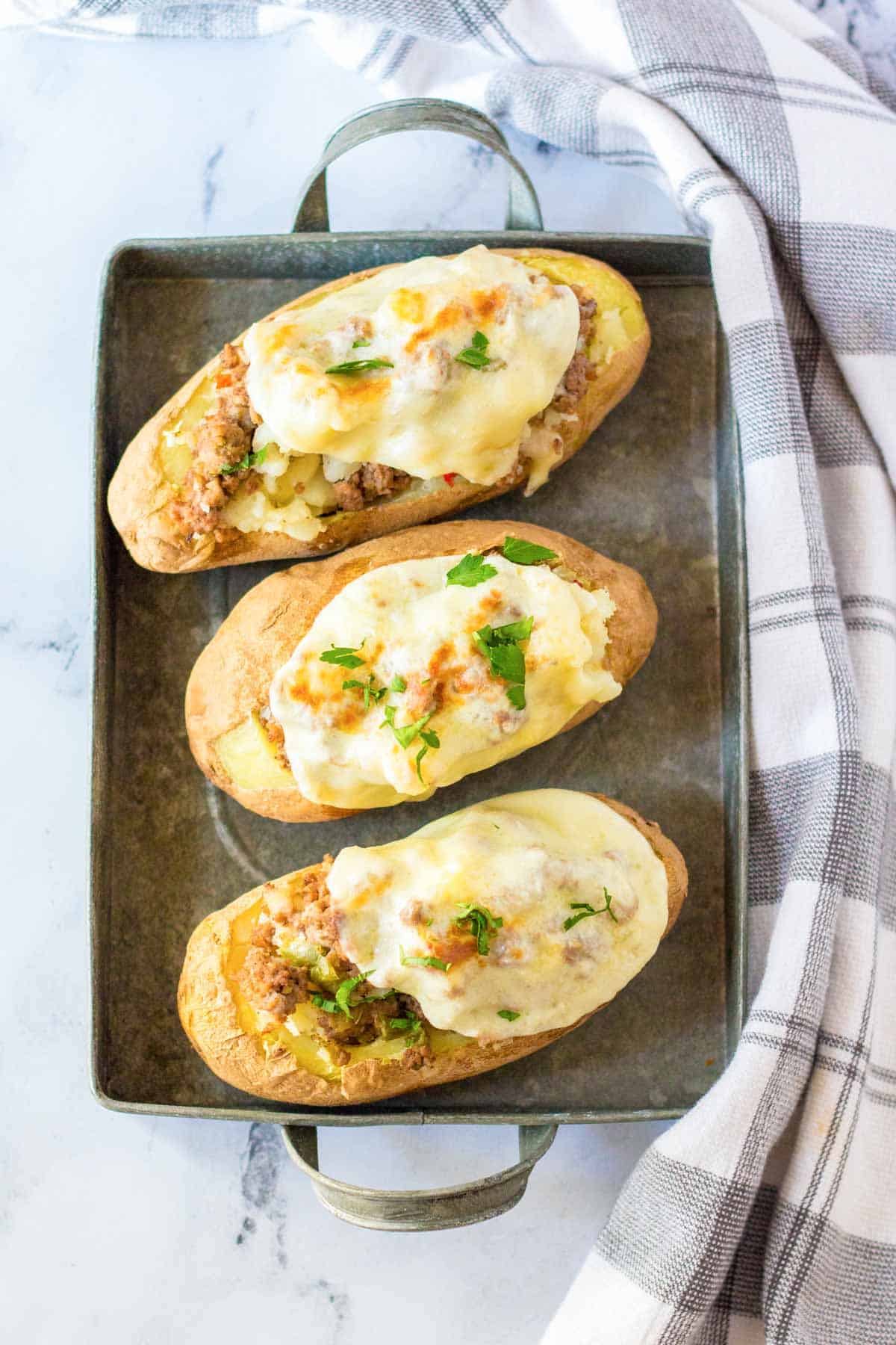 Three twice-baked potatoes with a beef and cheese filling on a metal tray.