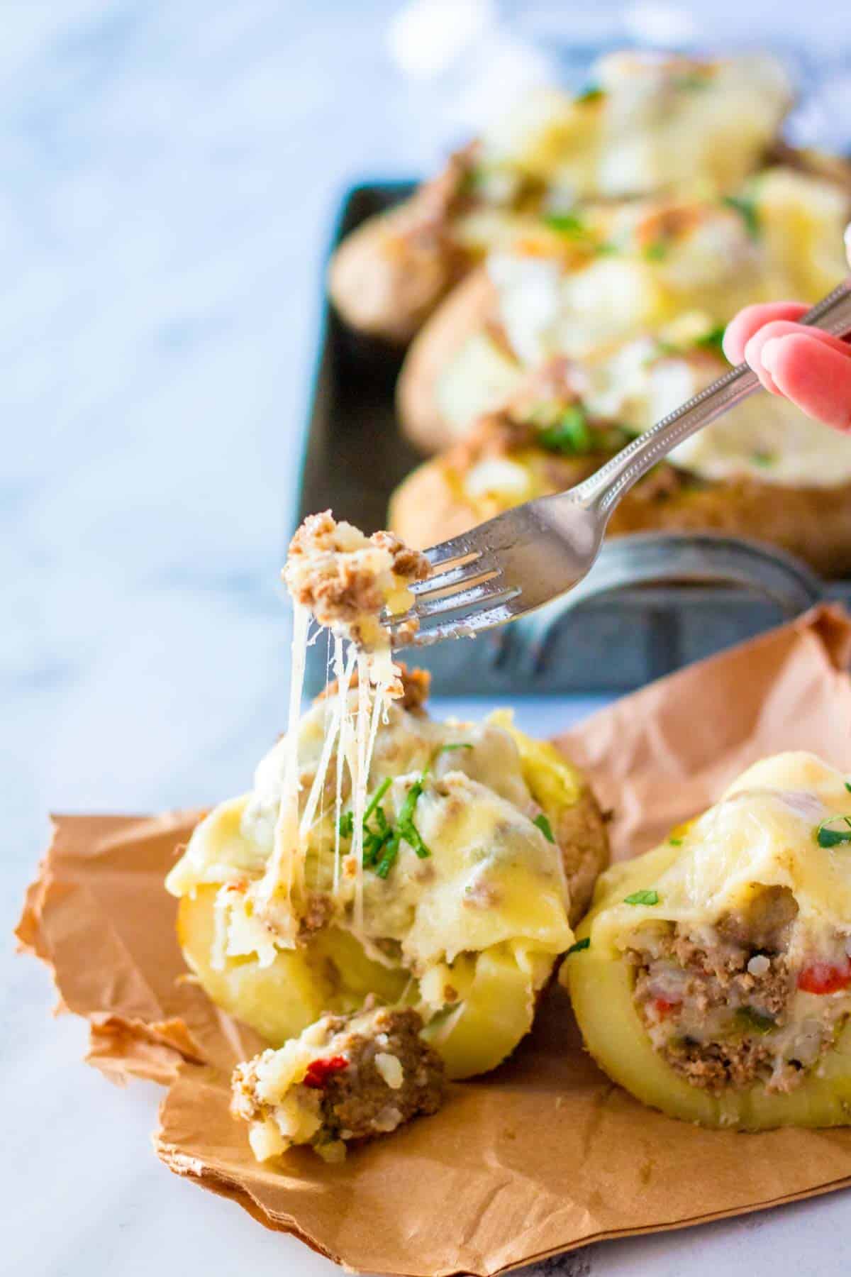 A fork picking up the Philly cheesesteak filling from a loaded baked potato cut in half.