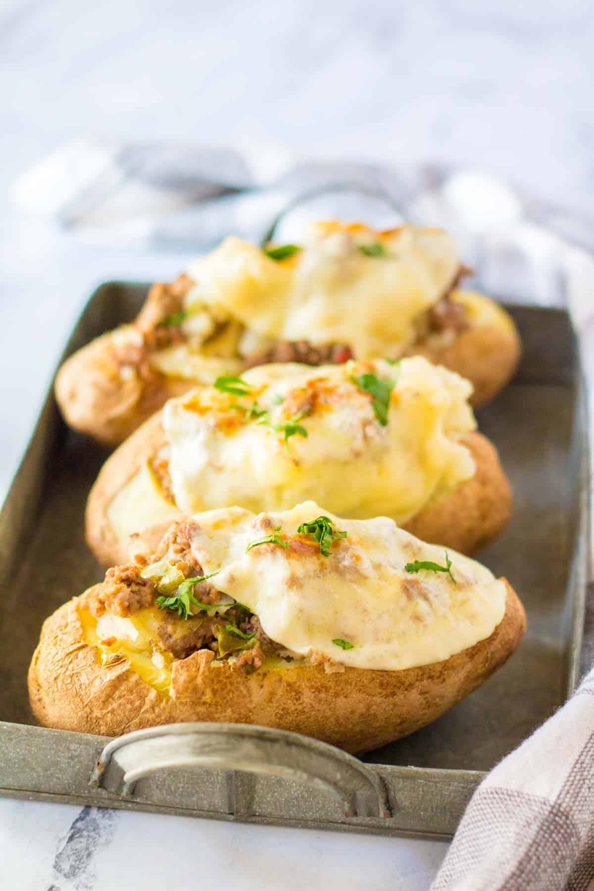 Three baked stuffed potatoes on a metal serving tray.