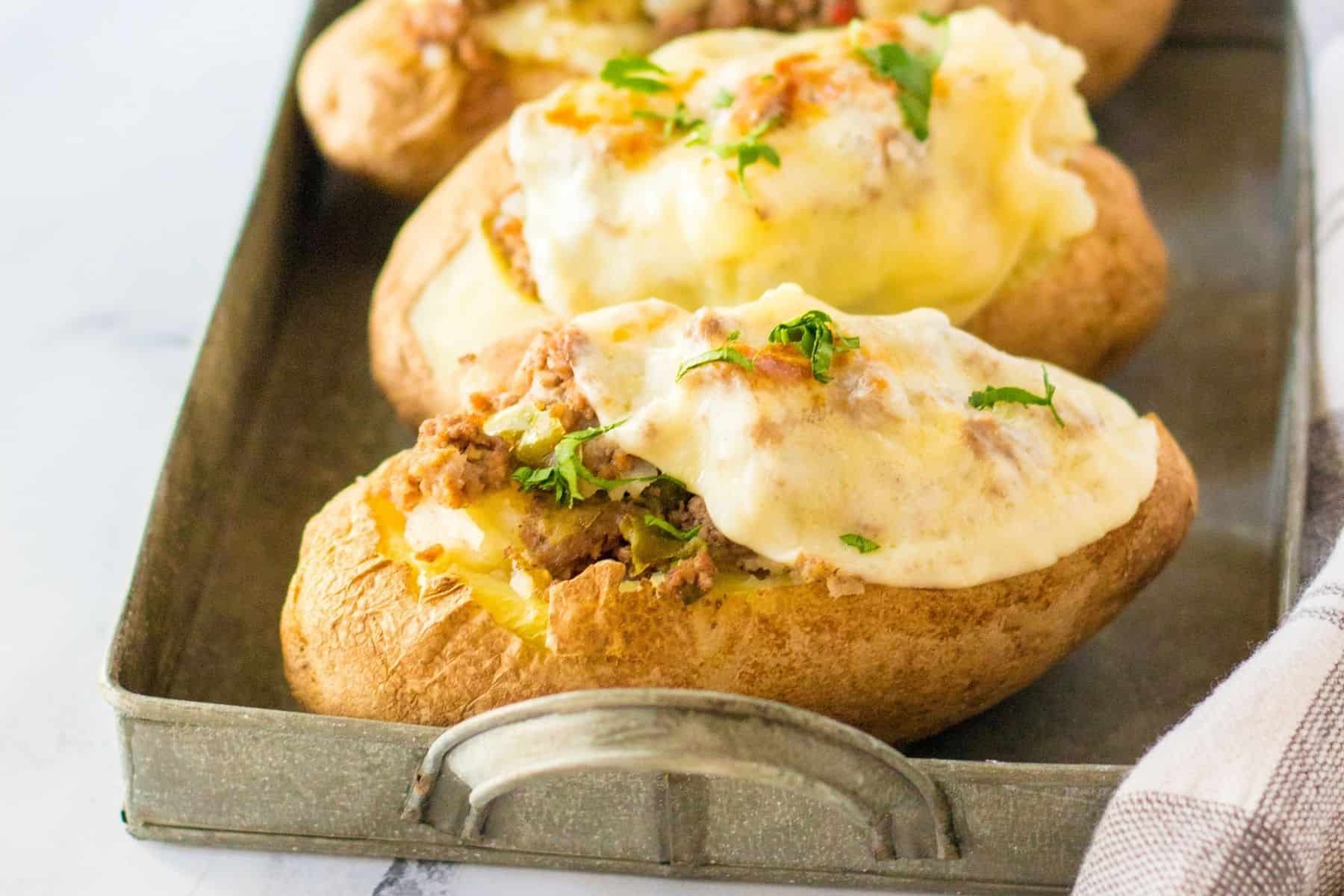 Stuffed baked potatoes on a serving tray with cheese melted on top.