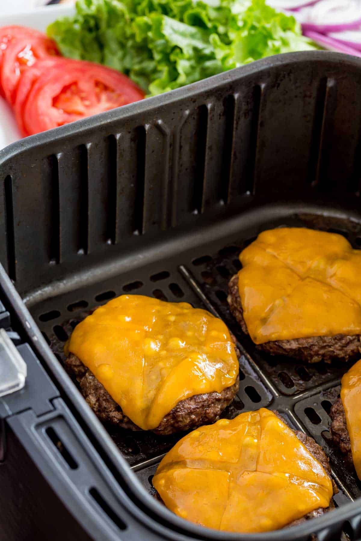 Cooked cheeseburgers in an air fryer basket.