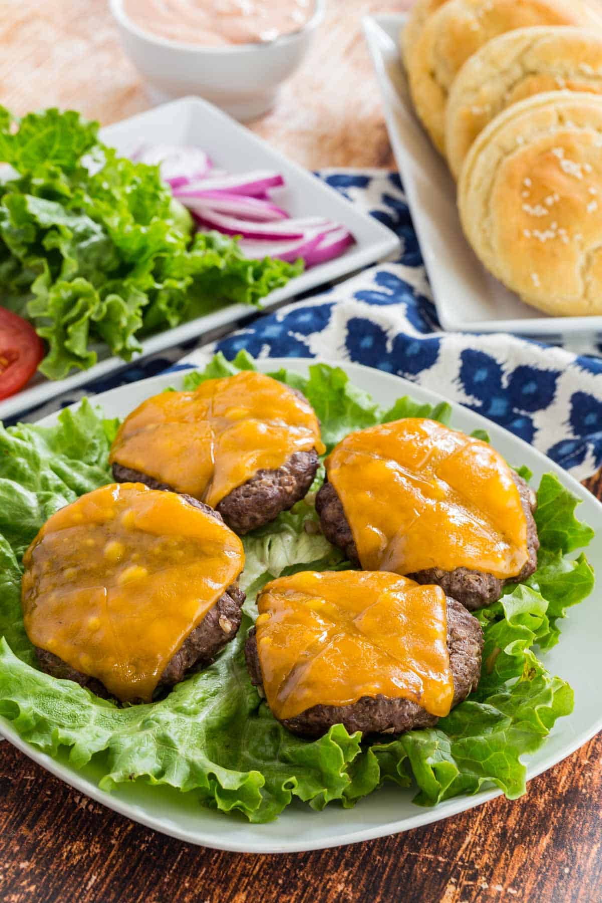 Four cooked cheeseburgers on a bed of lettuce on a plate