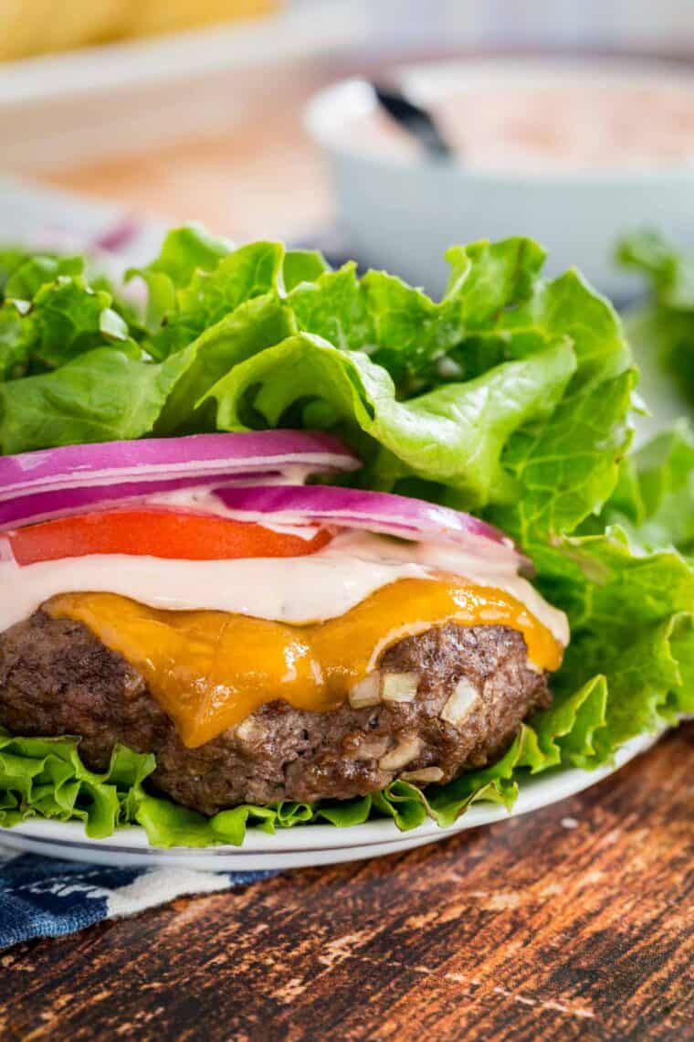 A cheeseburger in a lettuce wrap with burger sauce, tomatoes, and onion.
