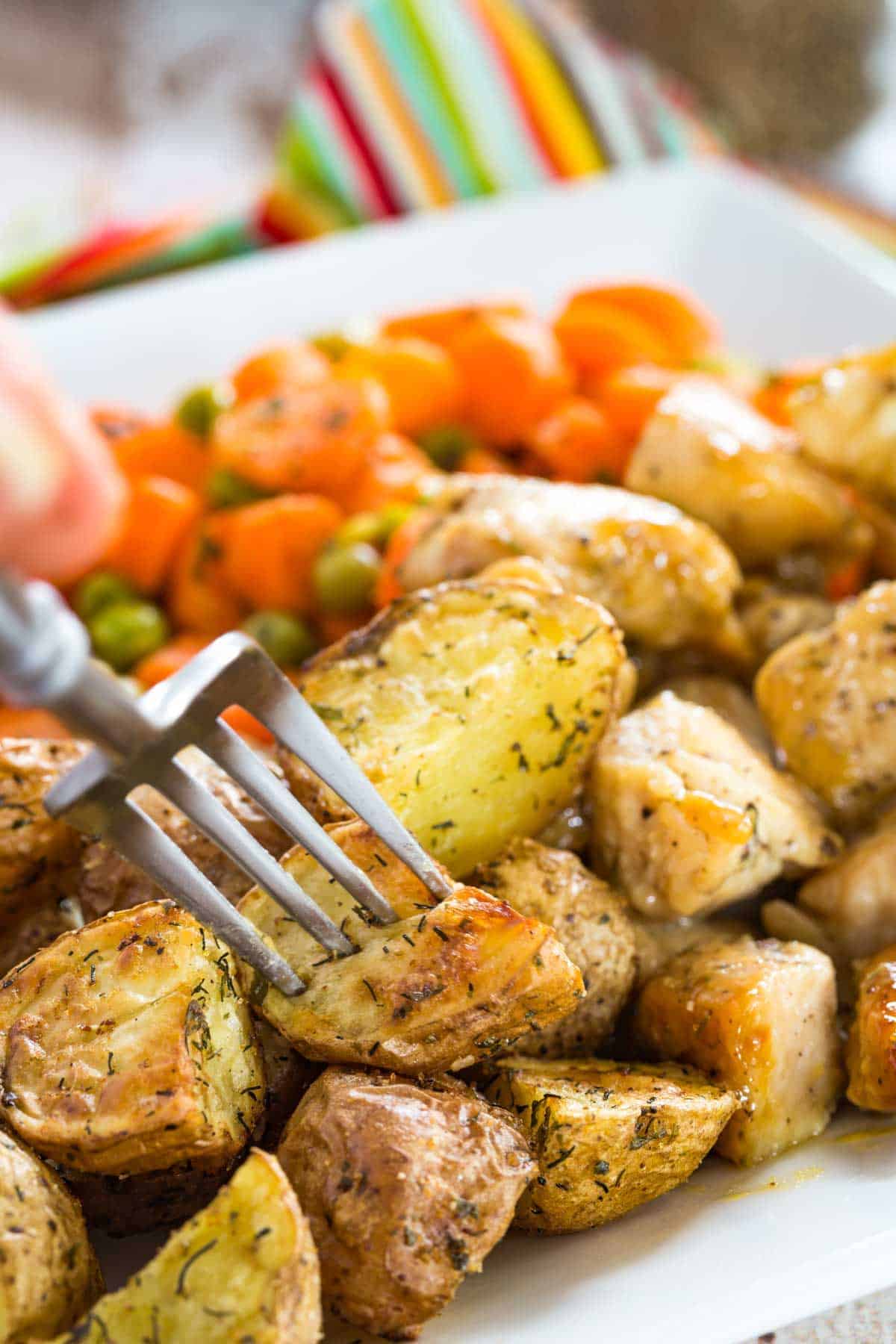 Ranch potatoes on a platter with cooked carrots and peas.