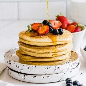 A stack of almond flour pancakes with syrup and berries on top.
