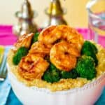 a bowl of cheesy quinoa topped with shrimp coated in barbecue sauce and broccoli.