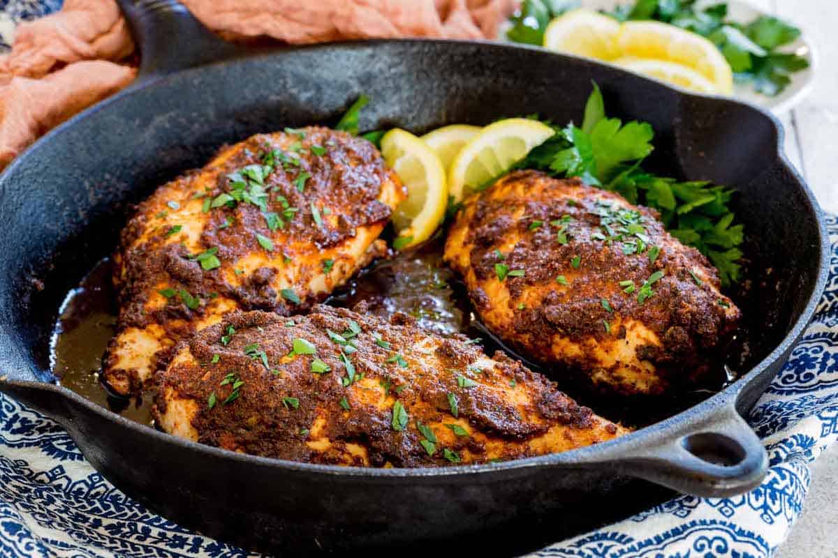 Baked blackened chicken breasts in a skillet with lemon and parsley.