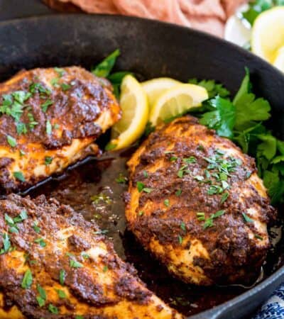 Baked blackened chicken breasts in a skillet with lemon and parsley.