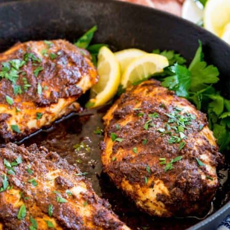 Baked blackened chicken breasts in a skillet with lemon and parsley.