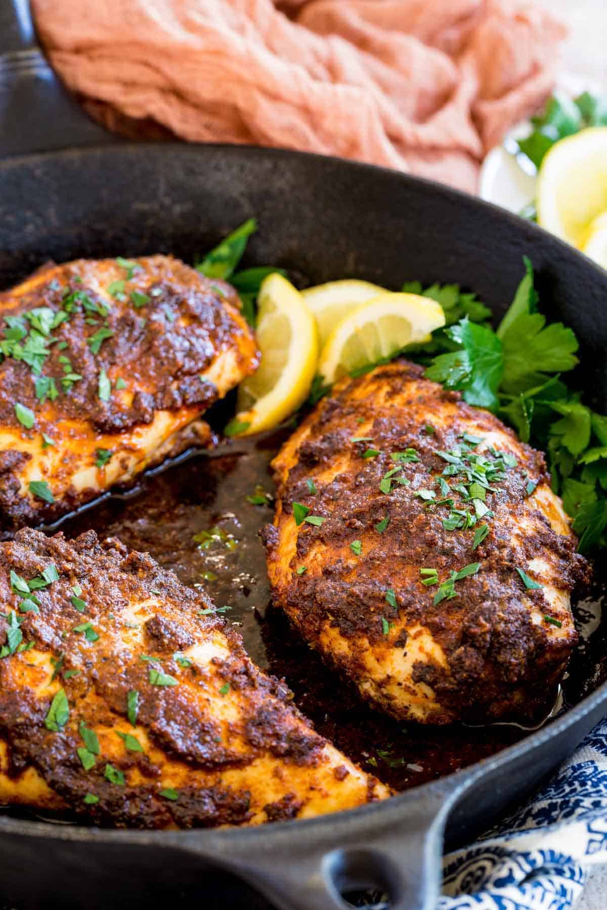 Baked blackened chicken breasts in a skillet with lemon and parsley.