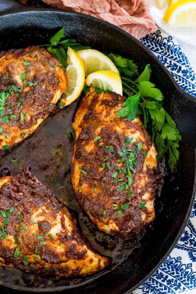 Baked blackened chicken breasts in a skillet with lemon and parsley.