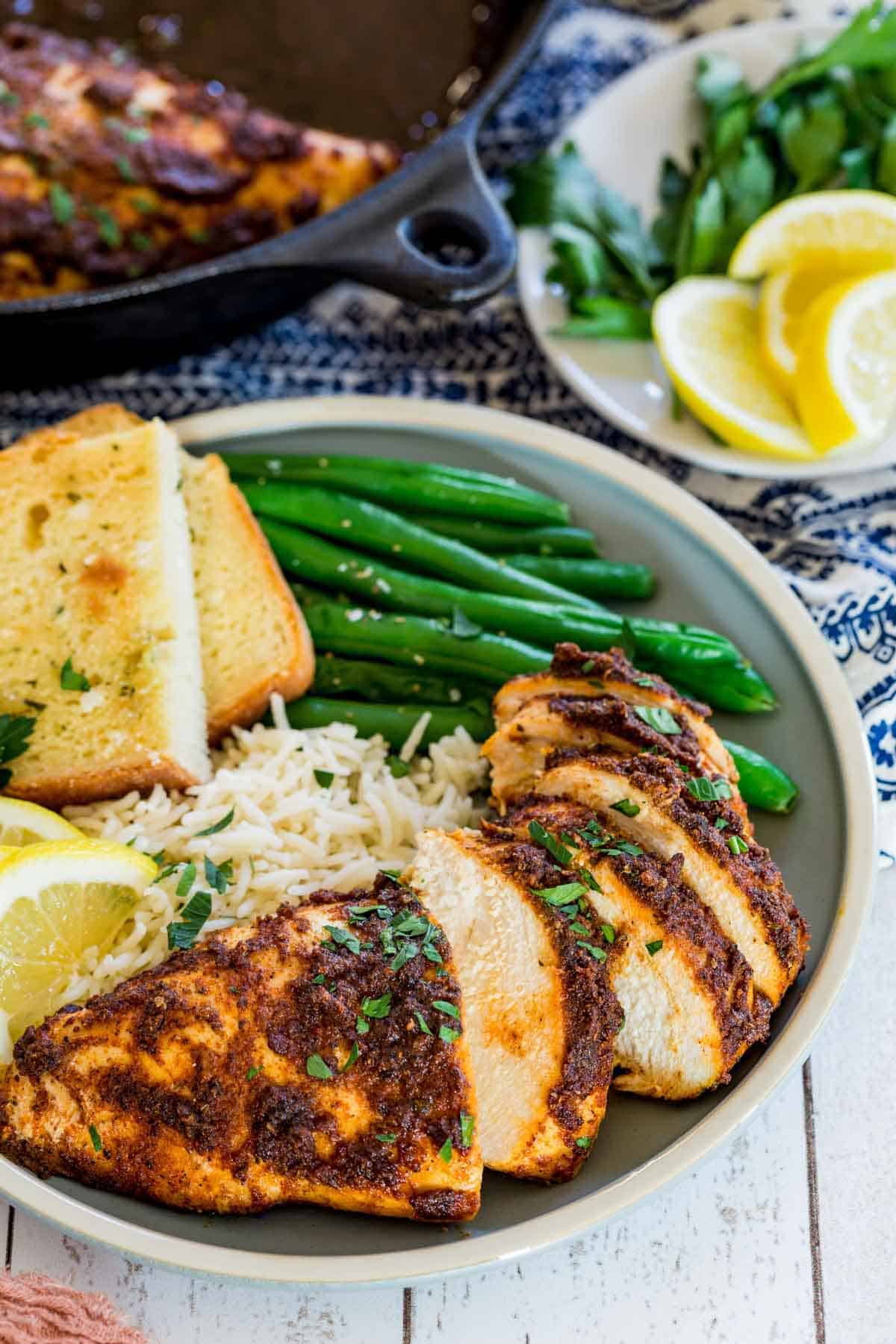 Juicy blackened chicken slices on a plate with green beans, rice, and toast slices.
