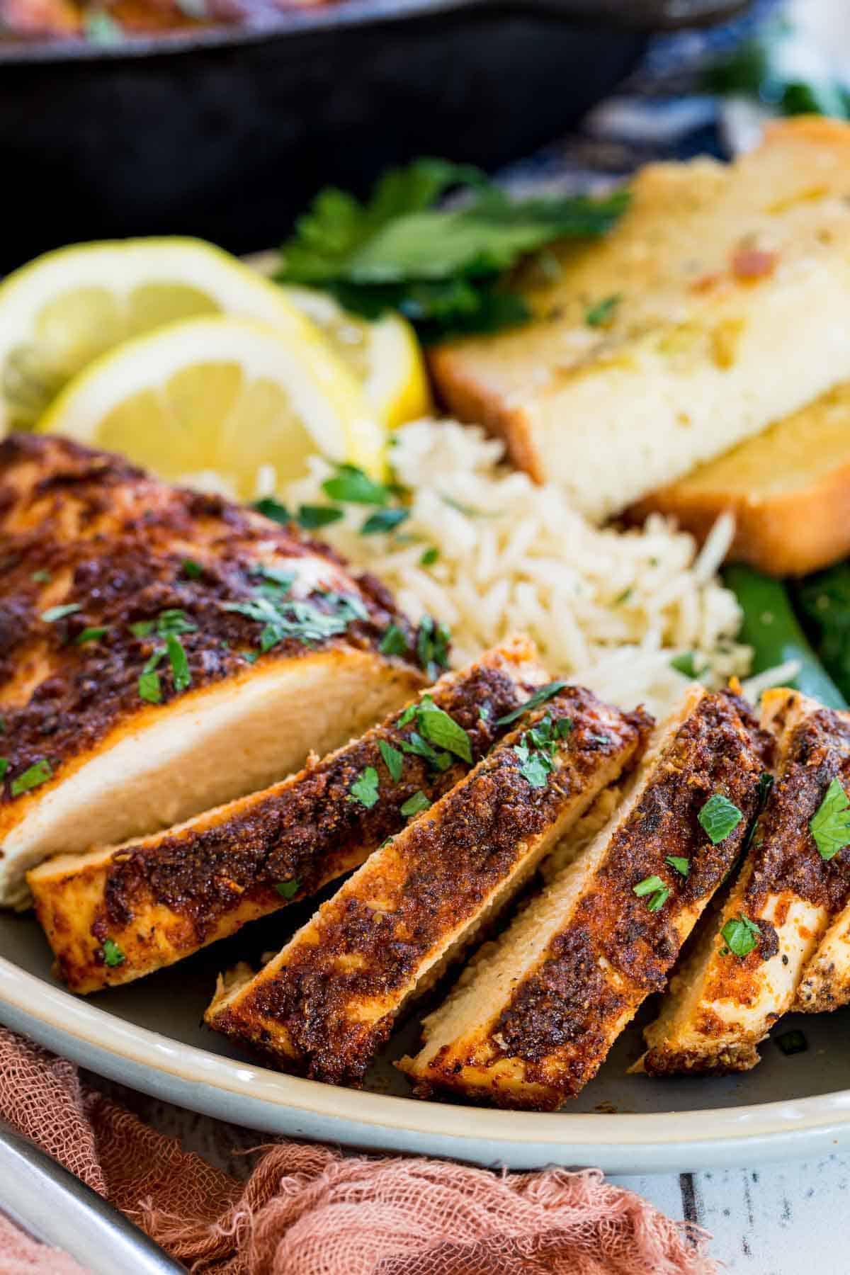 Juicy blackened chicken slices on a plate with green beans, rice, and toast slices.