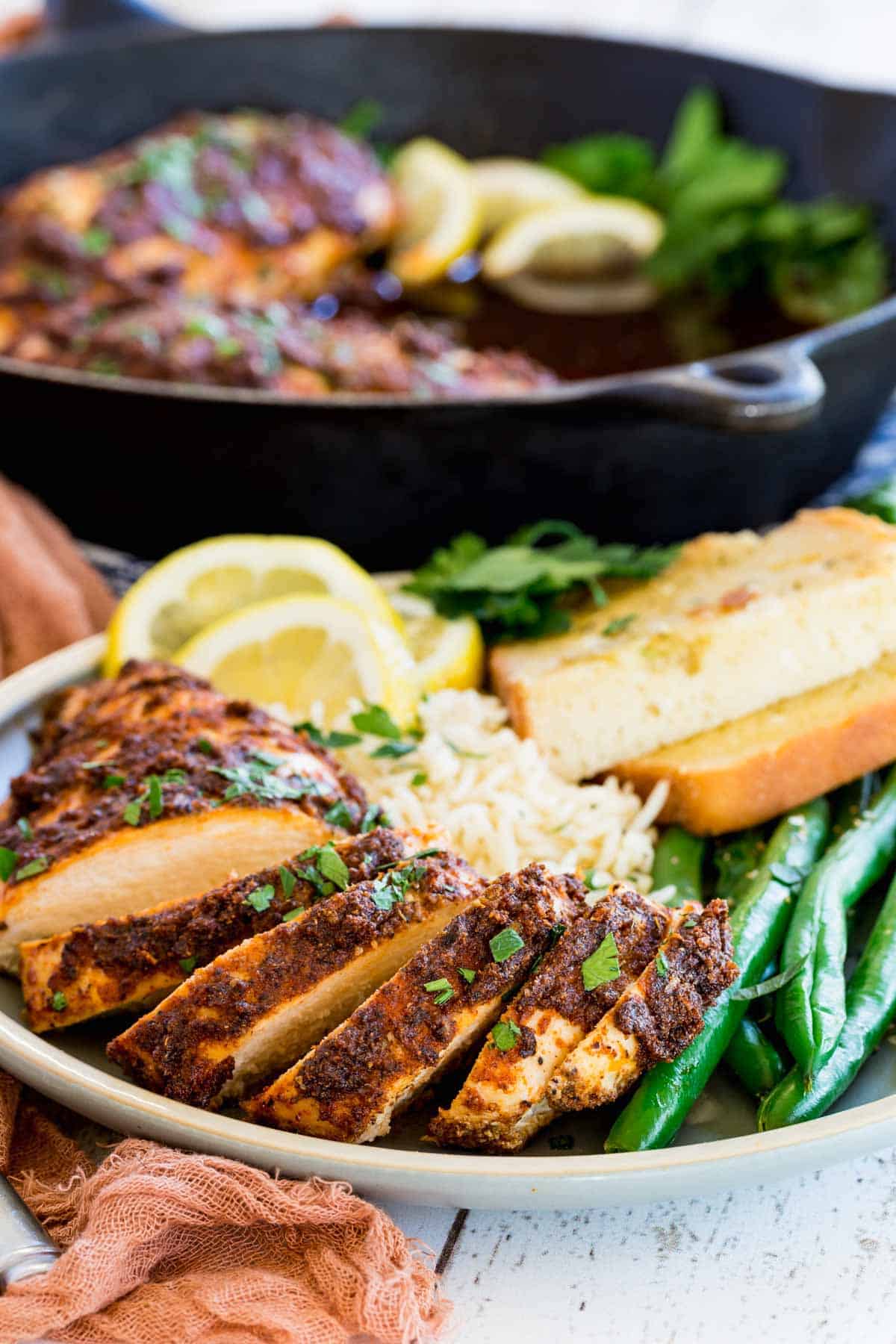 Juicy blackened chicken slices on a plate with green beans, rice, and toast slices.