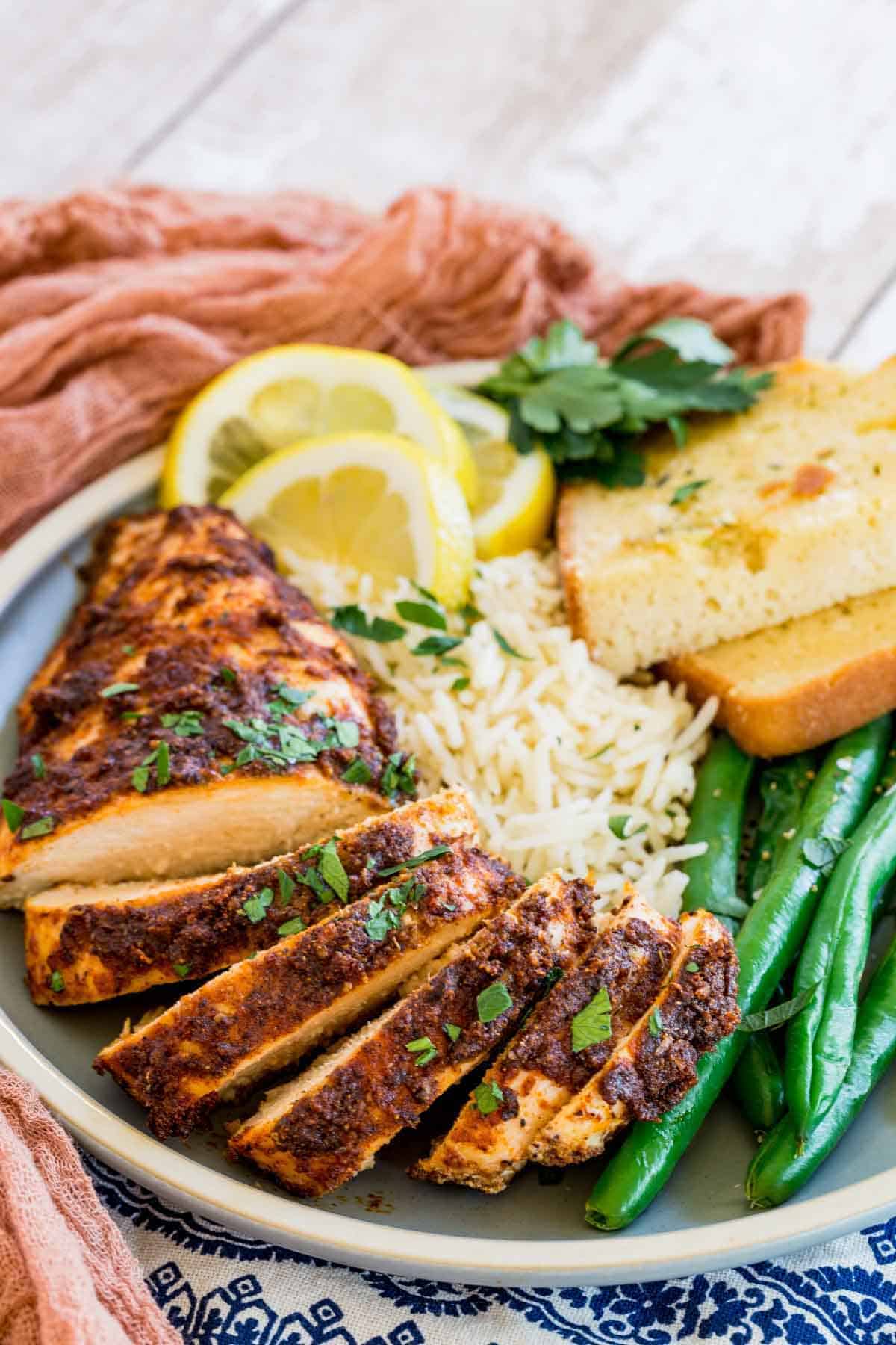 Juicy blackened chicken slices on a plate with green beans, rice, and toast slices.
