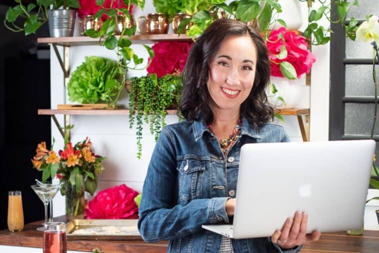 Woman standing in a kitchen holding a laptop.