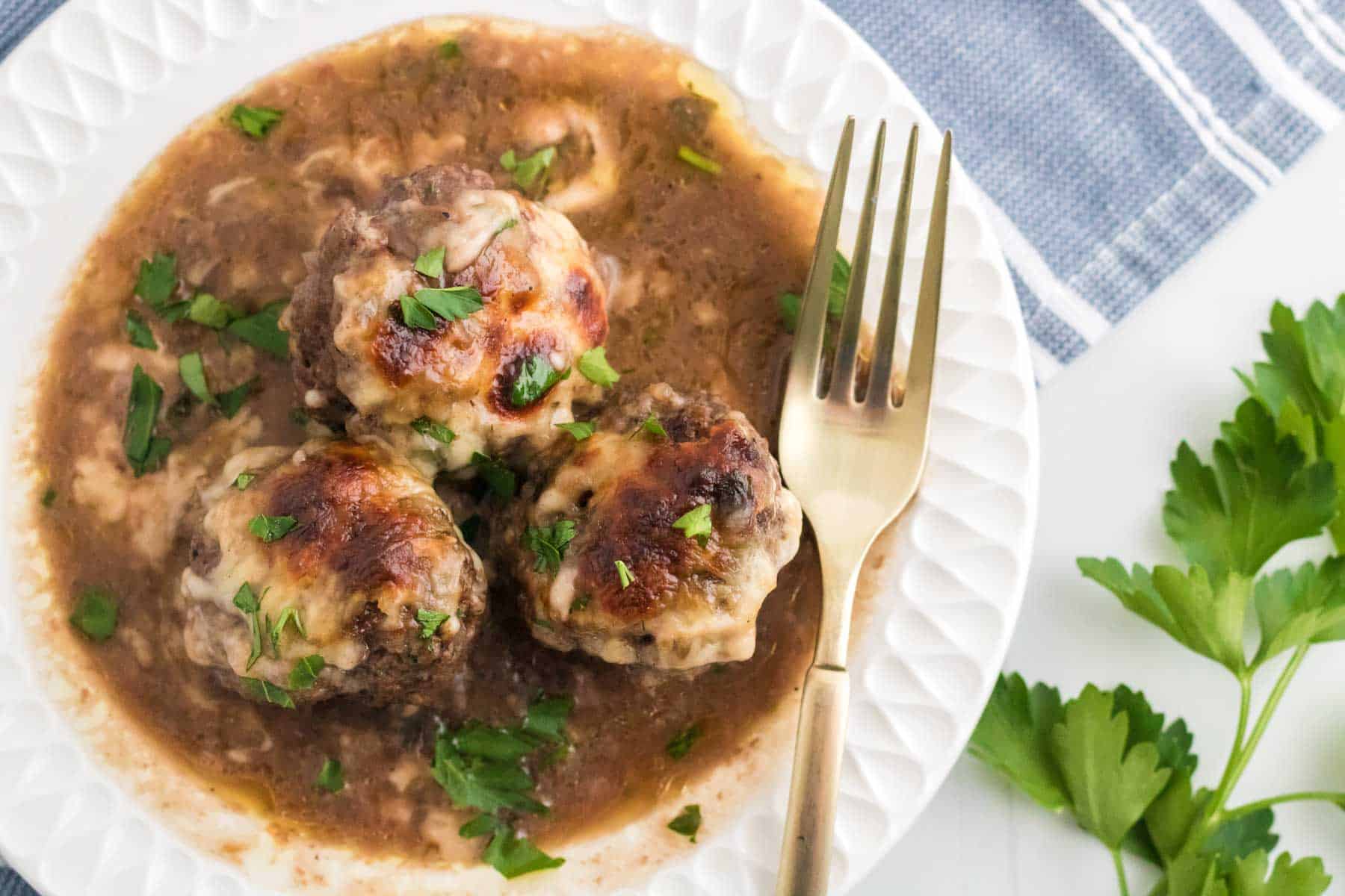 These cheese-topped meatballs on a plate with a fork.