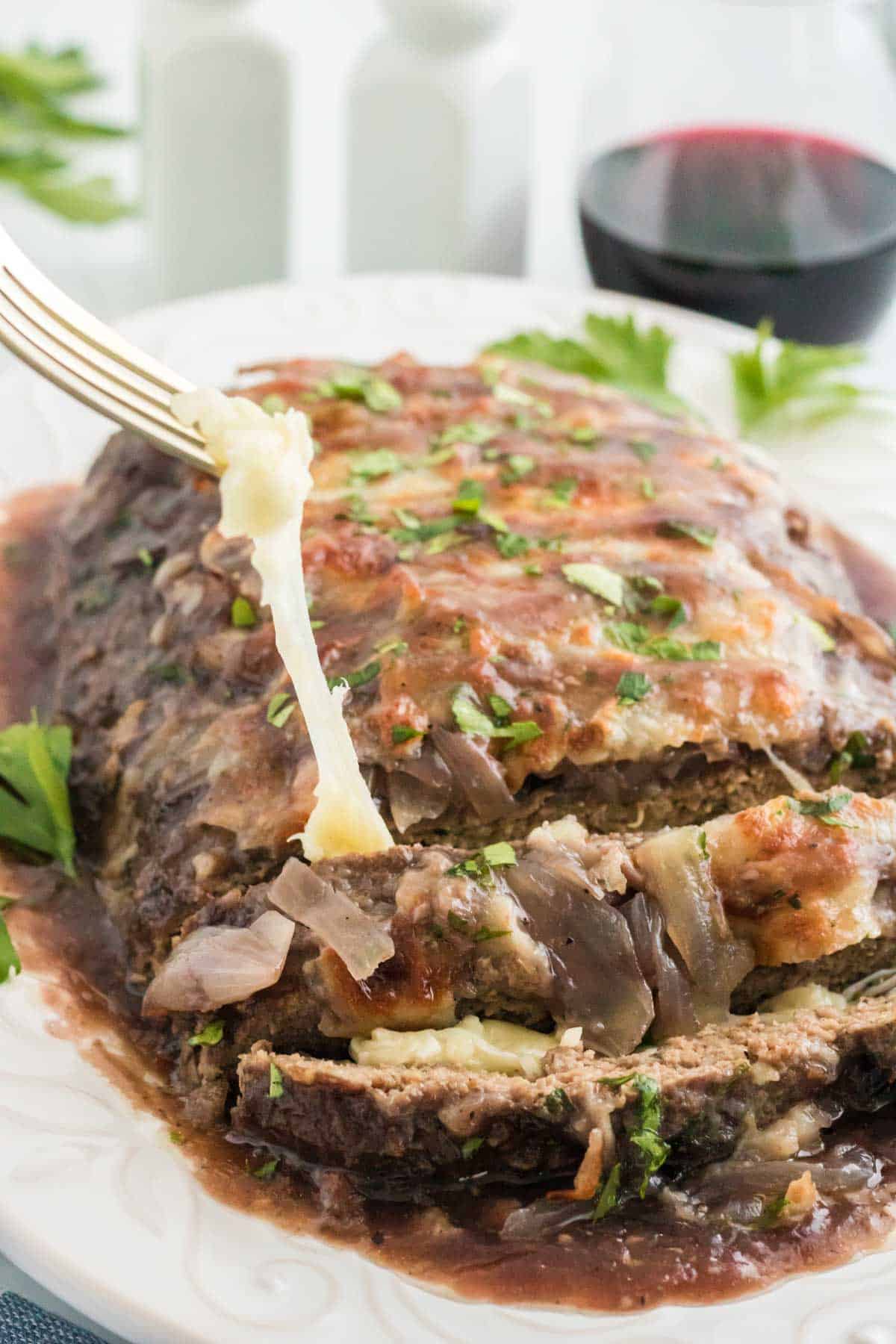 Mozzarella stuffed meatloaf on a serving platter with two slices cut off and a glass of wine in the background