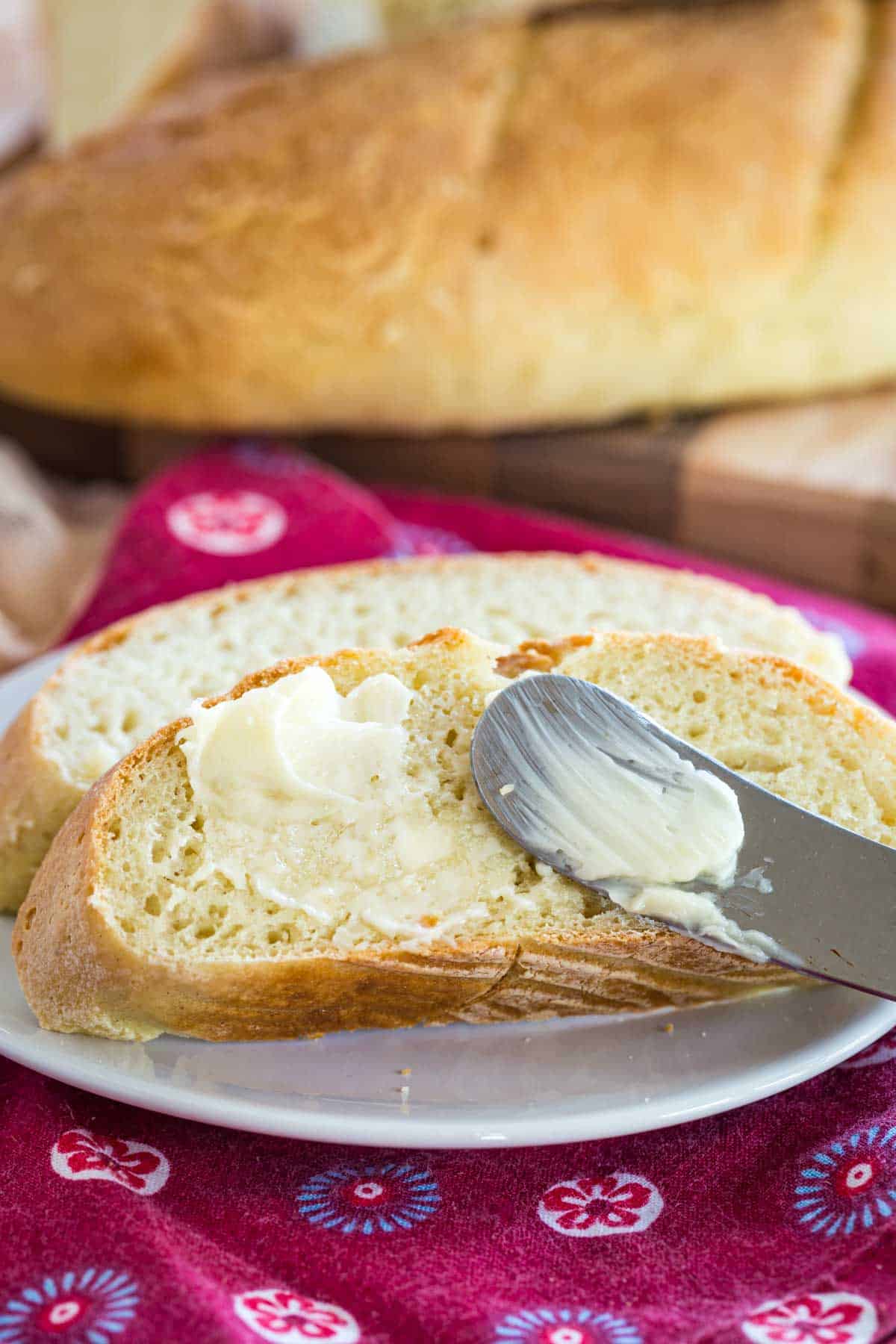 A buttered slice of gluten free French baguette with a butter knife.