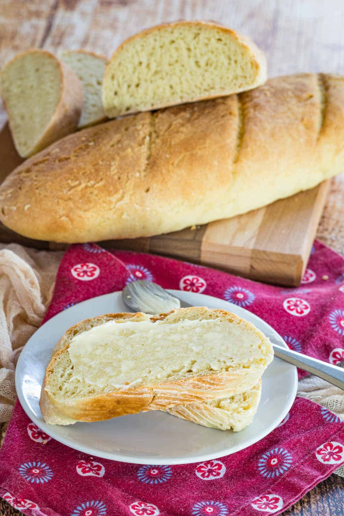 A buttered slice of gluten free French baguette next to a full loaf.