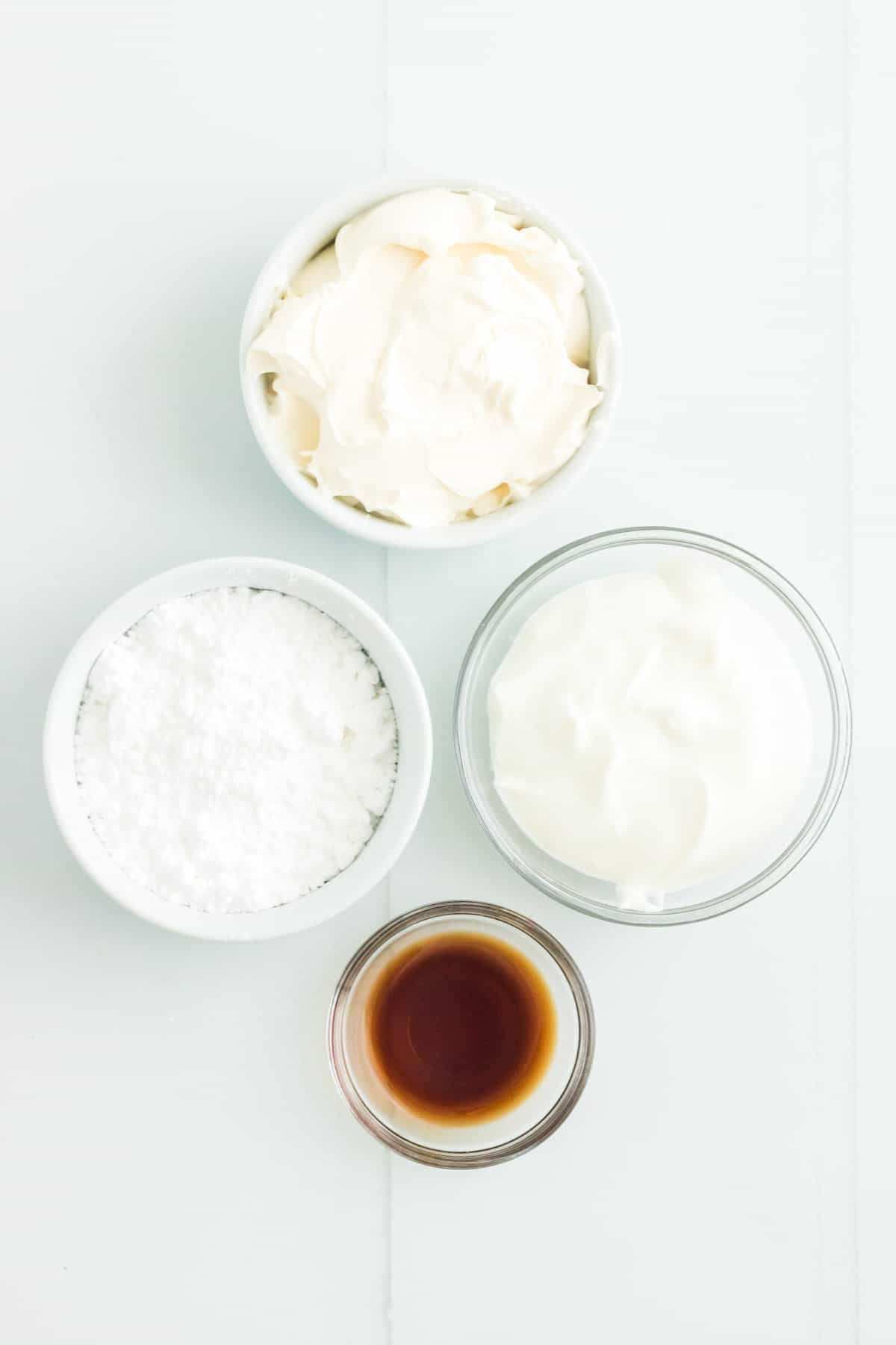 Powdered sugar, Greek yogurt, cream cheese and vanilla extract in small bowls on a countertop