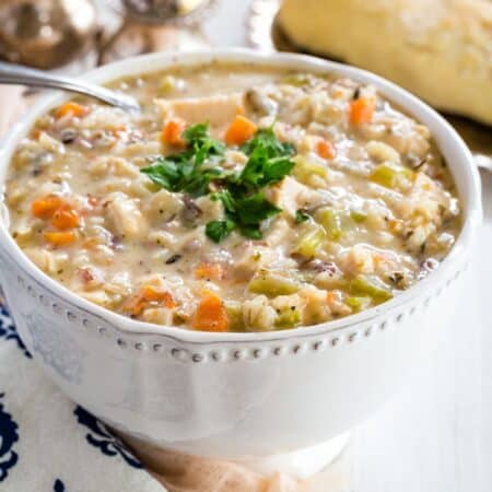 A bowl of chicken and wild rice soup garnished with parsley with a spoon in it.