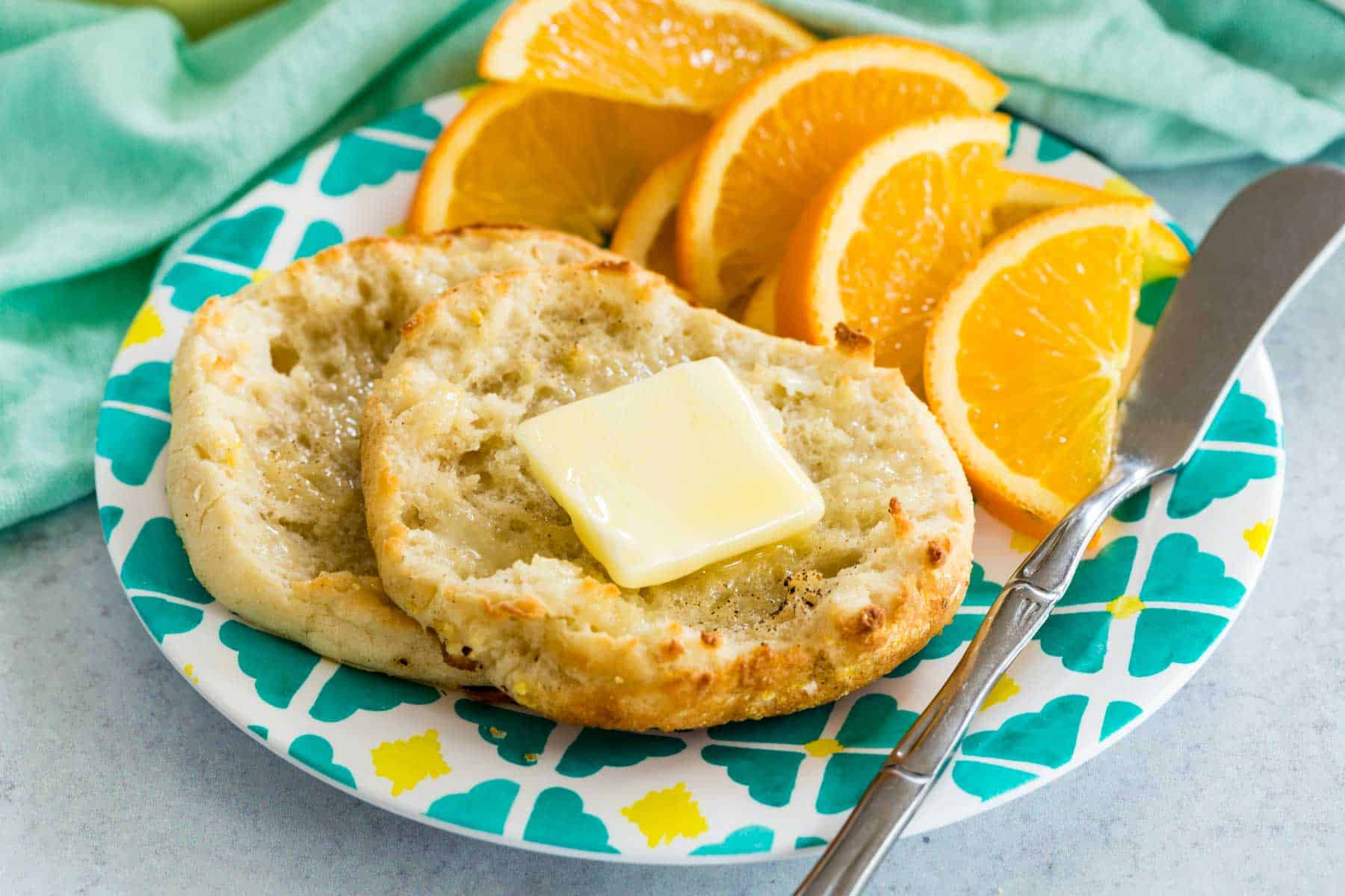 English muffins with a pat of butter in a plate with orange slices.