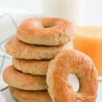 A stack of plain bagels with one leaning against the stack.