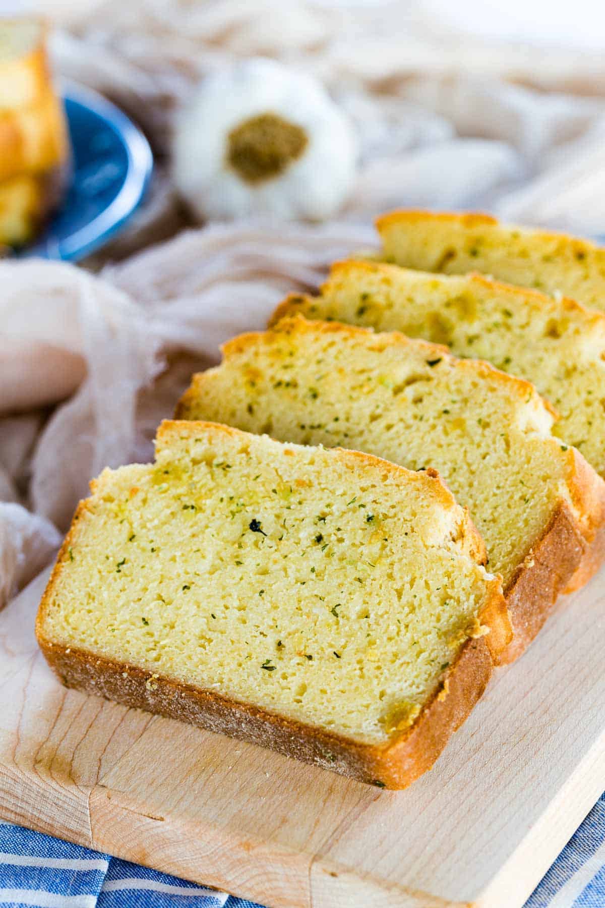 Slices of gluten-free Texas toast with butter and herbs on a wooden cutting board.