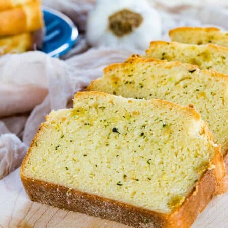 Slices of gluten-free Texas toast with butter and herbs on a wooden cutting board.