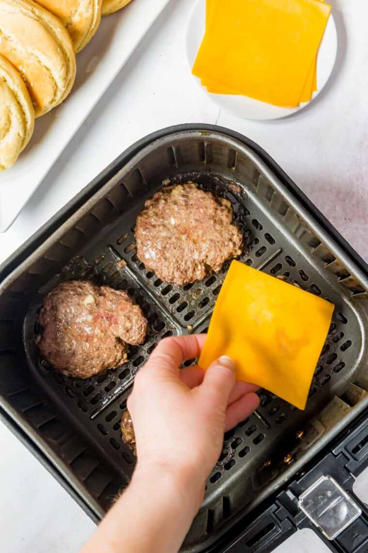 Placing cheese slices on partially cooked burgers in an air fryer.