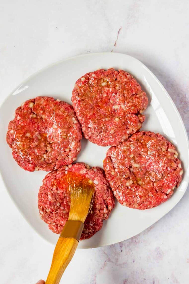 Brushing oil on the outside of raw burger patties.