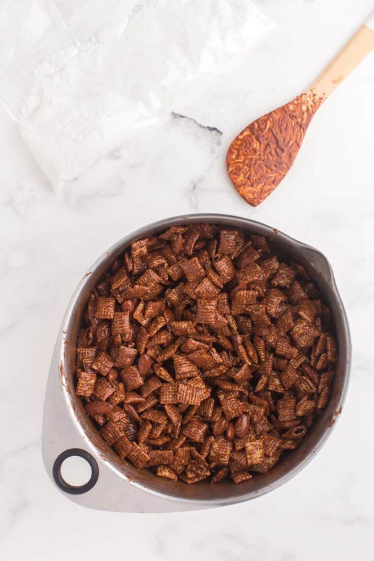 Chex cereal and almond coated in chocolate in a mixing bowl.