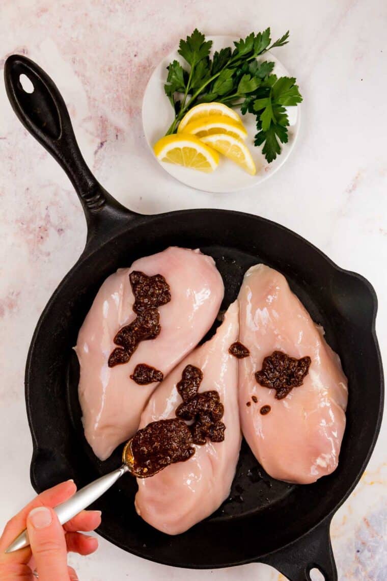 Blackening rub is added to the chicken breasts in a skillet.