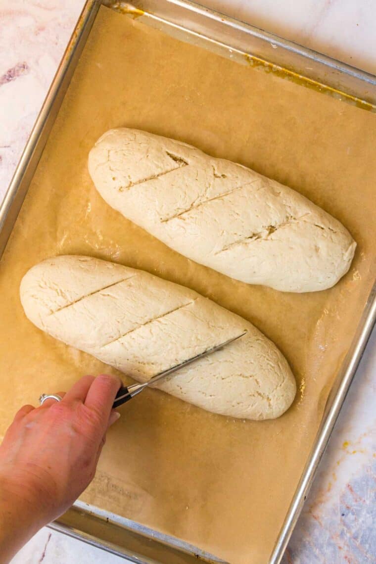 Two loaves of bread dough are scored with a knife.