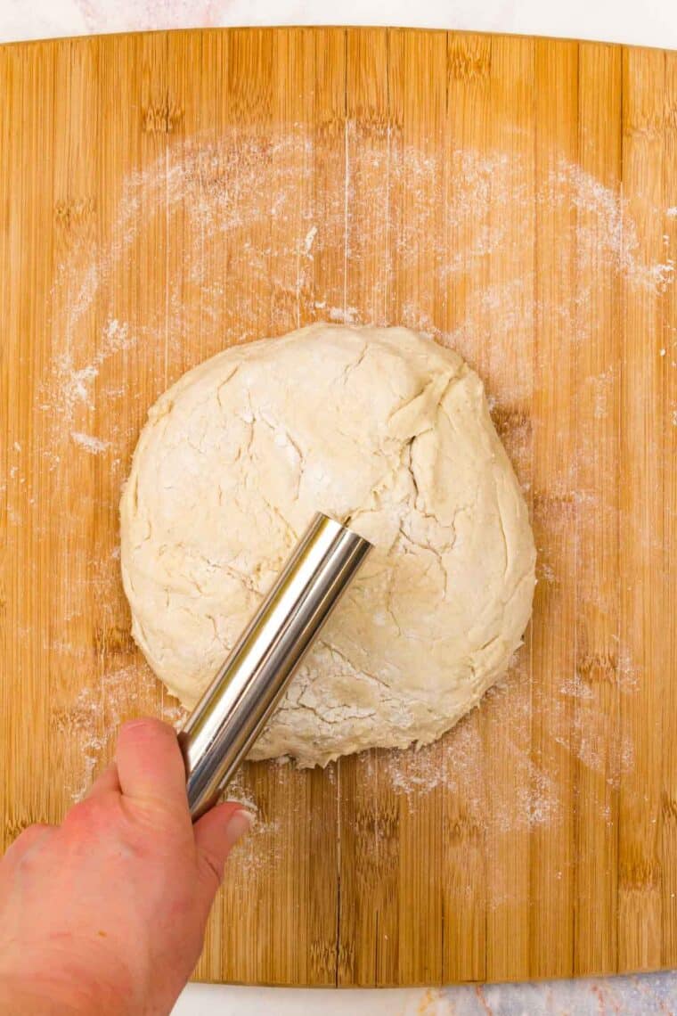 A hand uses a dough scraper to cut a ball of bread dough in half.