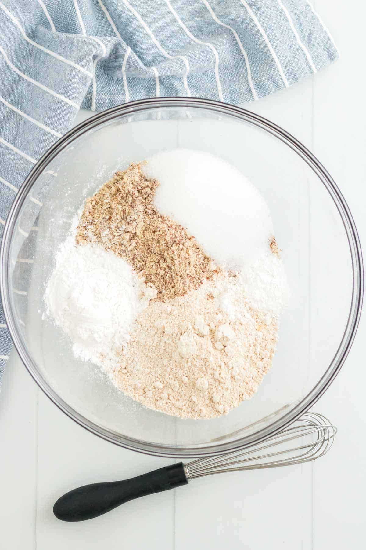 Oat flour, tapioca starch, sugar and the remaining dry ingredients inside of a mixing bowl next to a small whisk