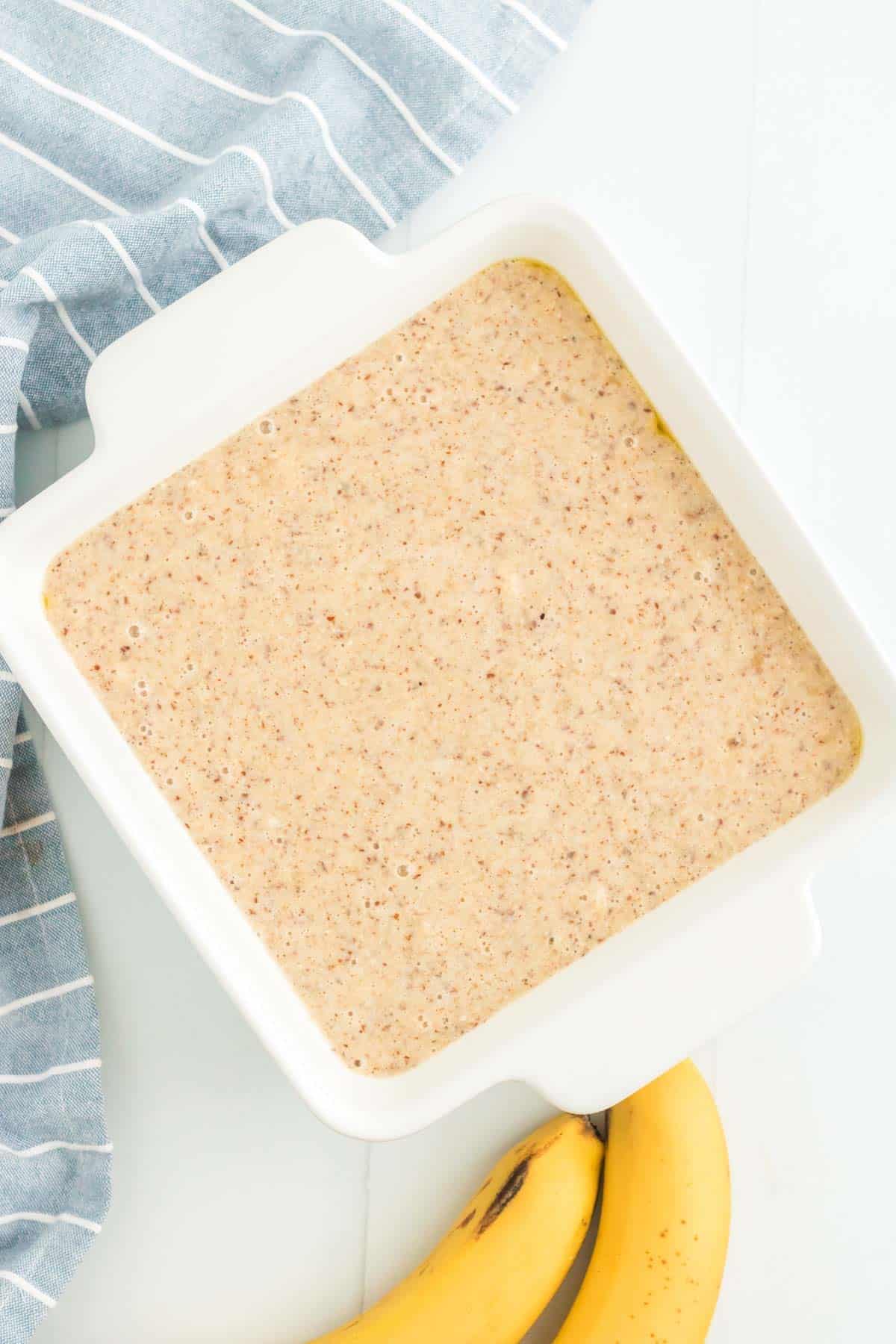 The cake batter inside of a greased cake pan with a handle on either side