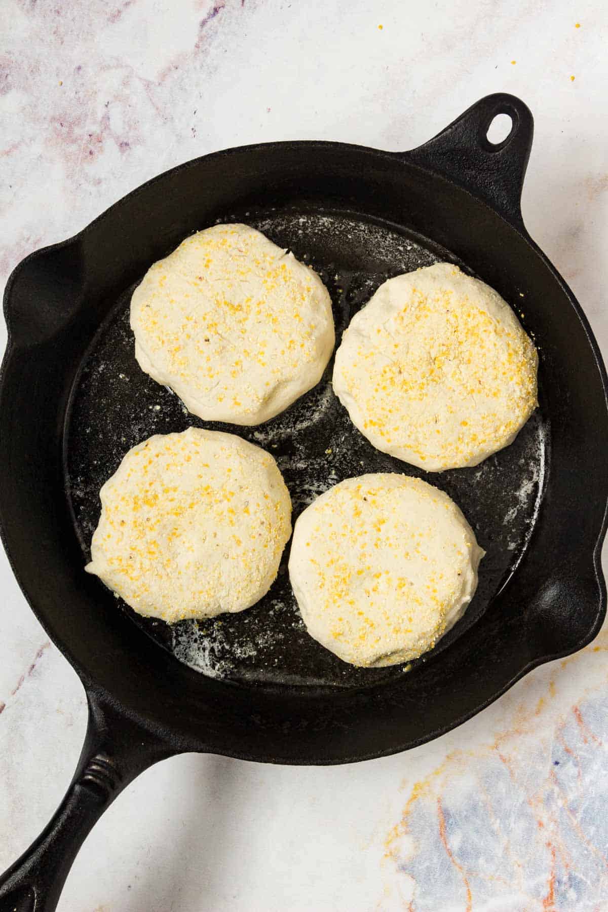 Gluten free English muffins cooking in a cast iron skillet.