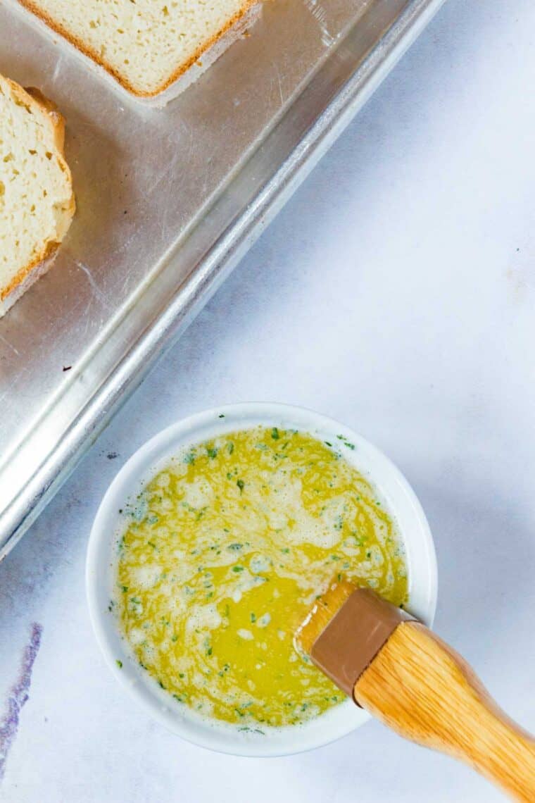 A bowl full of melted butter with garlic and seasonings with a brush.