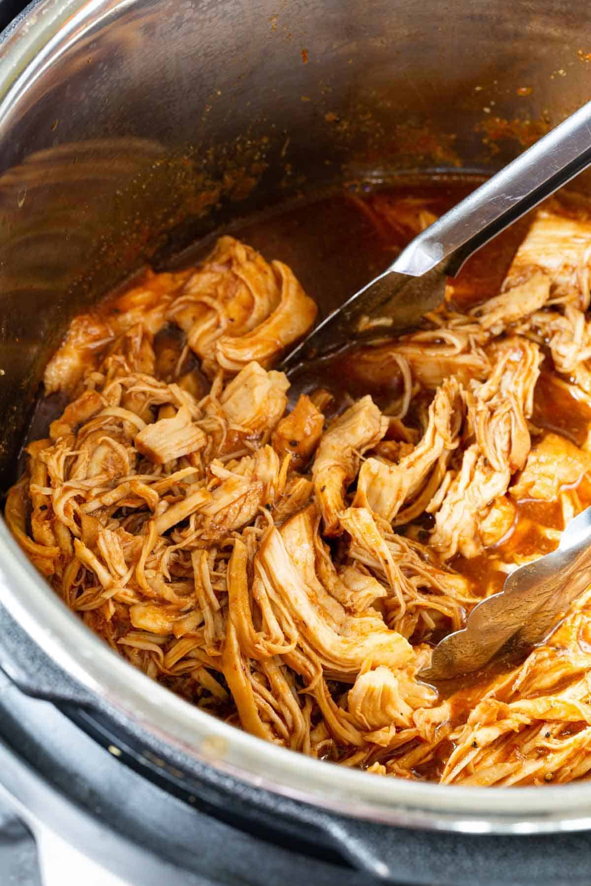 BBQ pulled chicken in the Instant Pot being stirred with tongs.