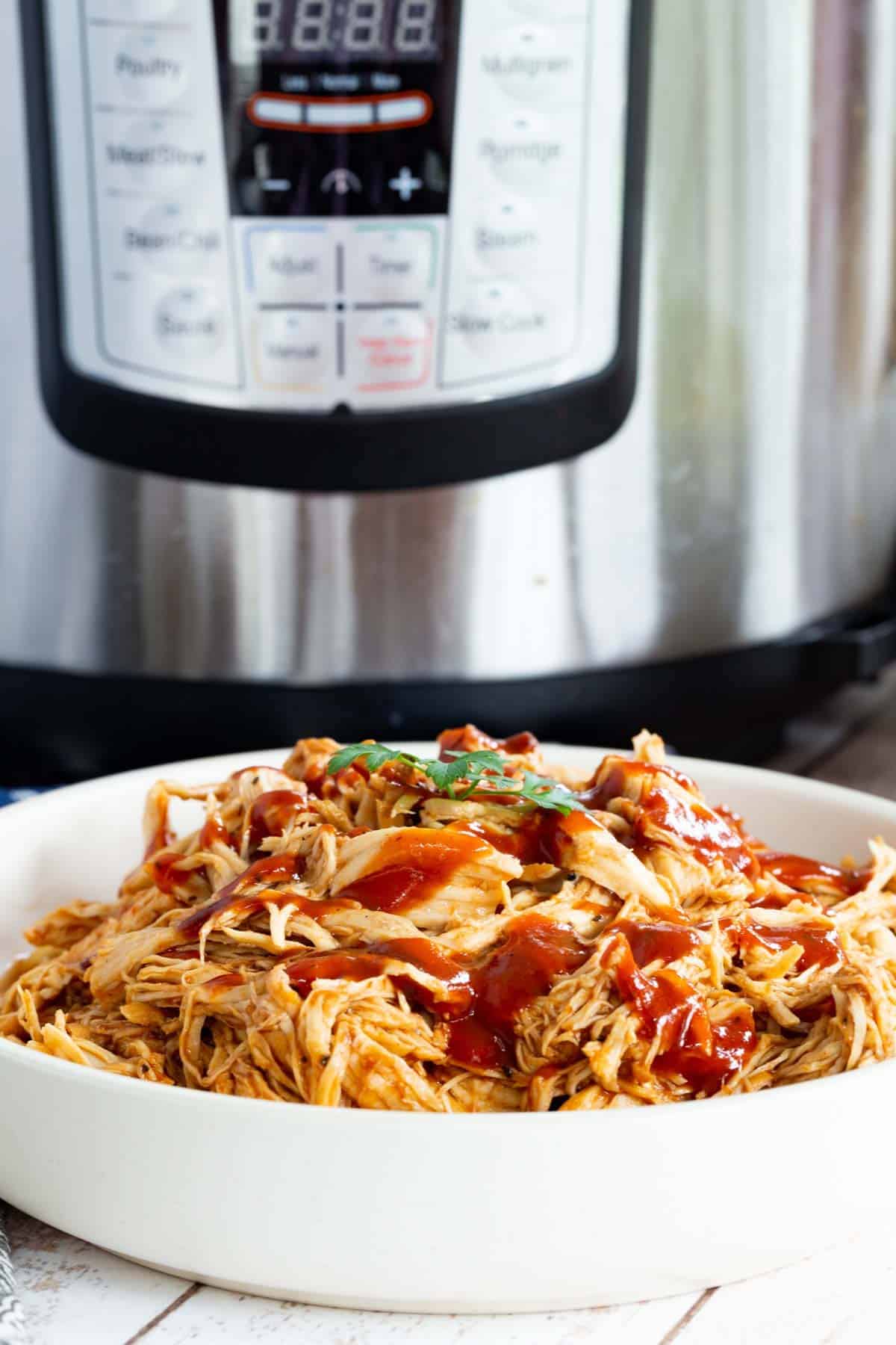 A bowl full of saucy BBQ pulled chicken with the Instant Pot in the background.