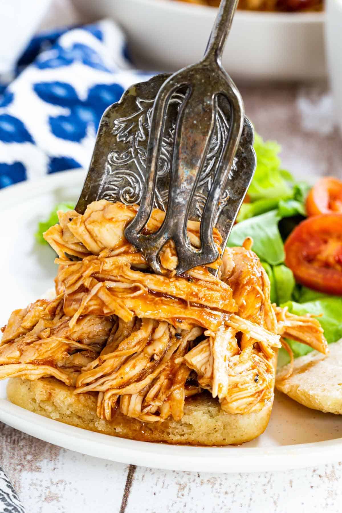 Pulled chicken is piled on top of a bread bun.