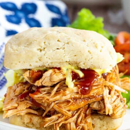 A BBQ pulled chicken sandwich on a plate with a side salad.